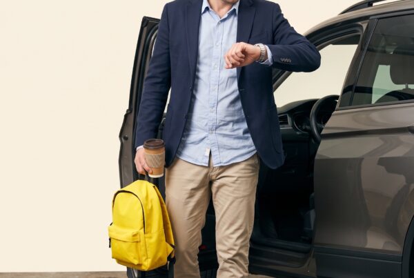 Portrait studio : parent pressé regardant sa montre devant son SUV portière ouverte, cartable jaune à la main